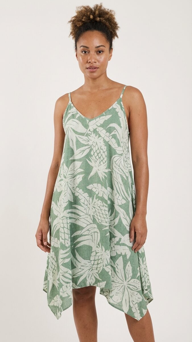 Close view of a sage green and white tropical print handkerchief hem dress on a spaghetti strap silhouette